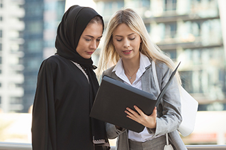 A woman shows another woman in a hijab documents. 